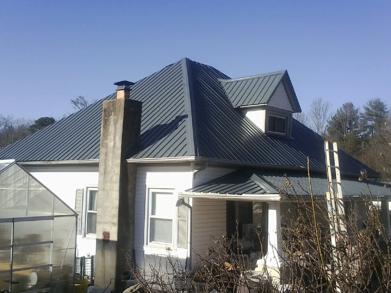 Dark blue standing seam metal roof on a white farmhouse with dormer — Slate & Tile Roof Repair by Roofing Brothers in Alstead