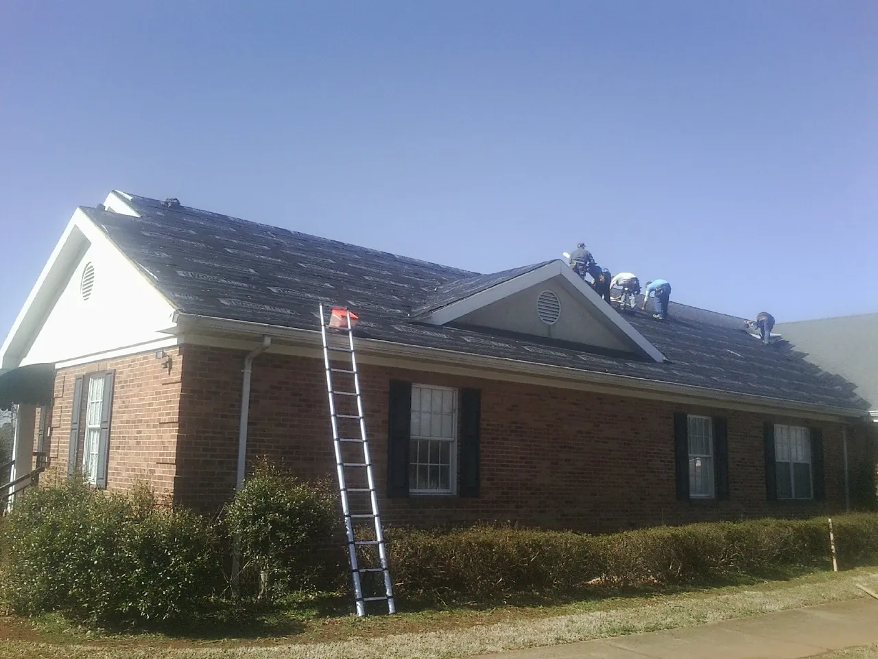 Crew tearing shingles off a brick ranch roof with a ladder set — Metal Roof Repair work by our crew in Alstead