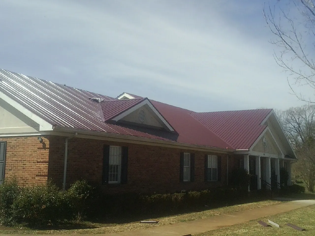 Red metal roof with gabled entries on a long brick building, from a Hail Damage Roof Repair job in Alstead