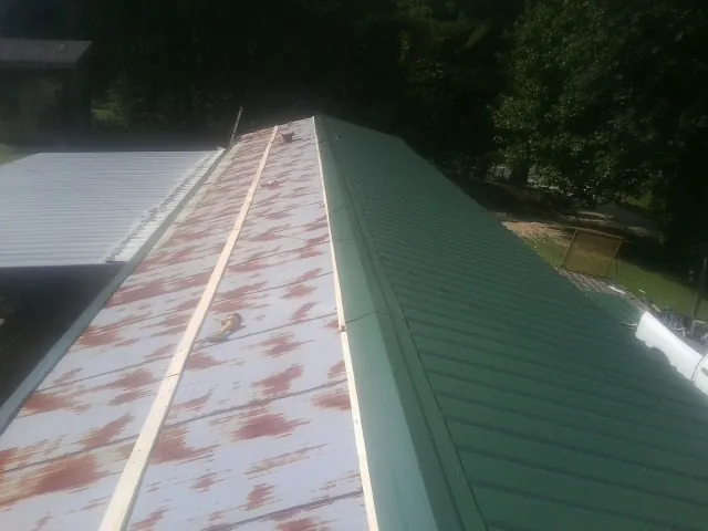 Old rusted panels beside newly installed green metal roofing — Wind Damage Roof Repair by Roofing Brothers in Alstead
