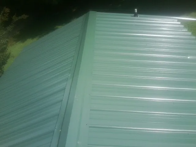 New green metal panels meeting at the ridge of a roof — Flat Roof Repair work by our crew in Alstead