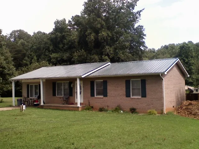 Gray metal roof on a brick ranch house with a side carport in Alstead