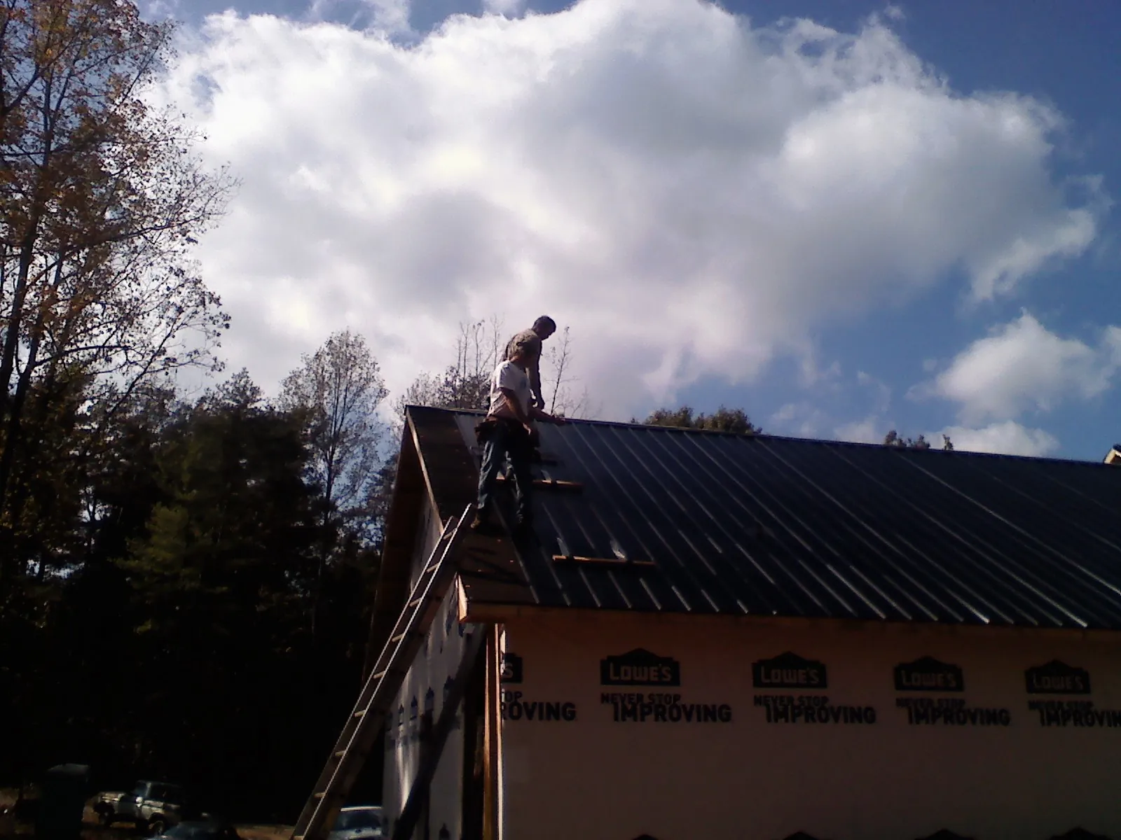 Roofer fastening dark metal panels high against a cloudy sky, from a Roof Inspection job in Alstead