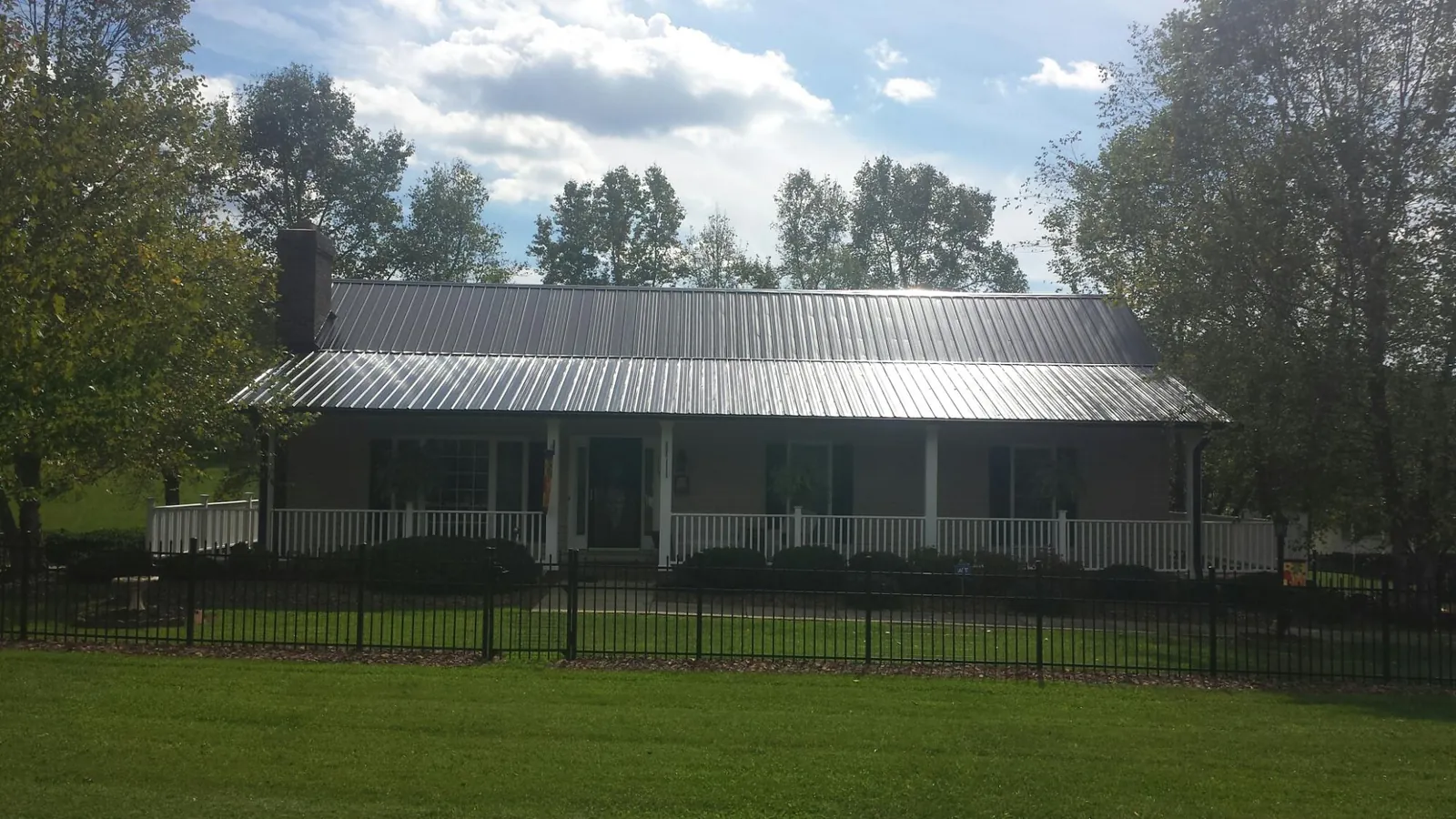 Gray metal roof on a brick ranch with a full width front porch — Gutter Guard Installation work by our crew in Alstead